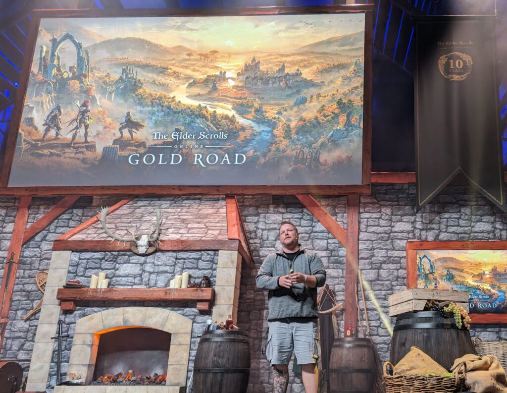 Rich Lambert standing onstage with the Gold Road keyart on two screens behind him.